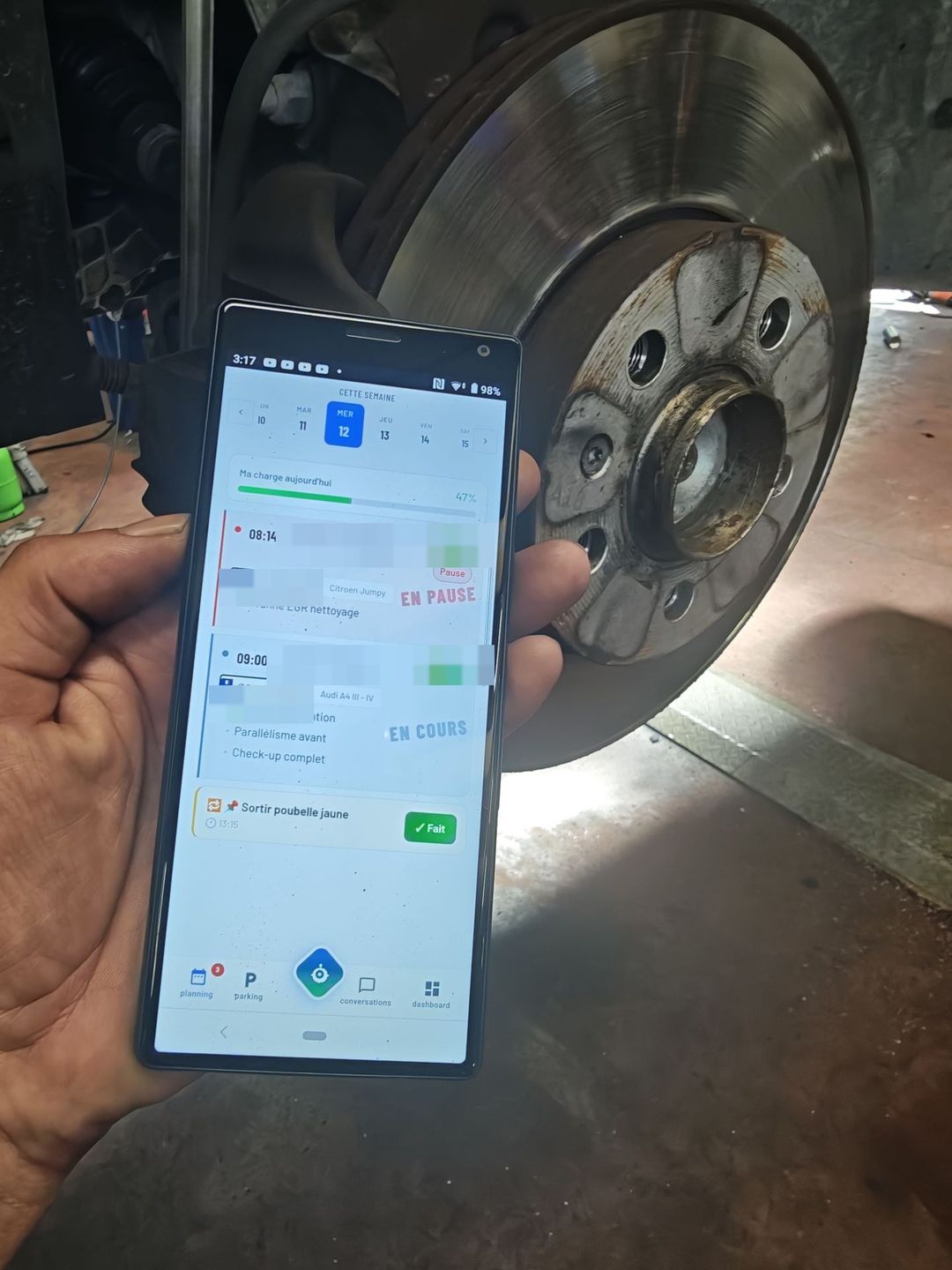 Planning du jour de l'application technicien Axium tenu devant un disque de frein : charge de journée, rendez-vous et tâche récurrente